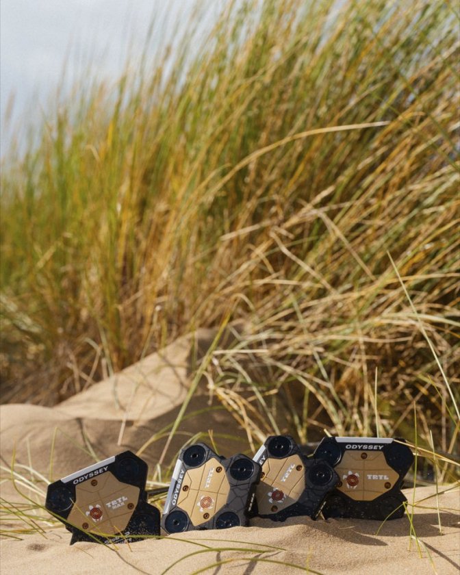 Quatre putters Odyssey TRTL dans le sable devant des herbes de dune