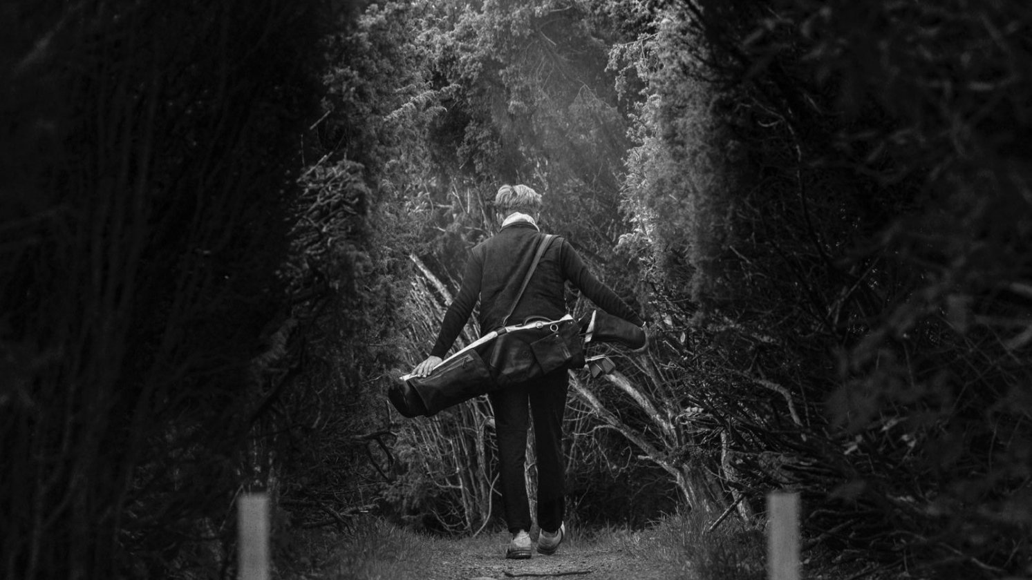 Golfeur marchant sur un chemin bordé d'arbres, un sac Sunday Pine Coast sur l'épaule
